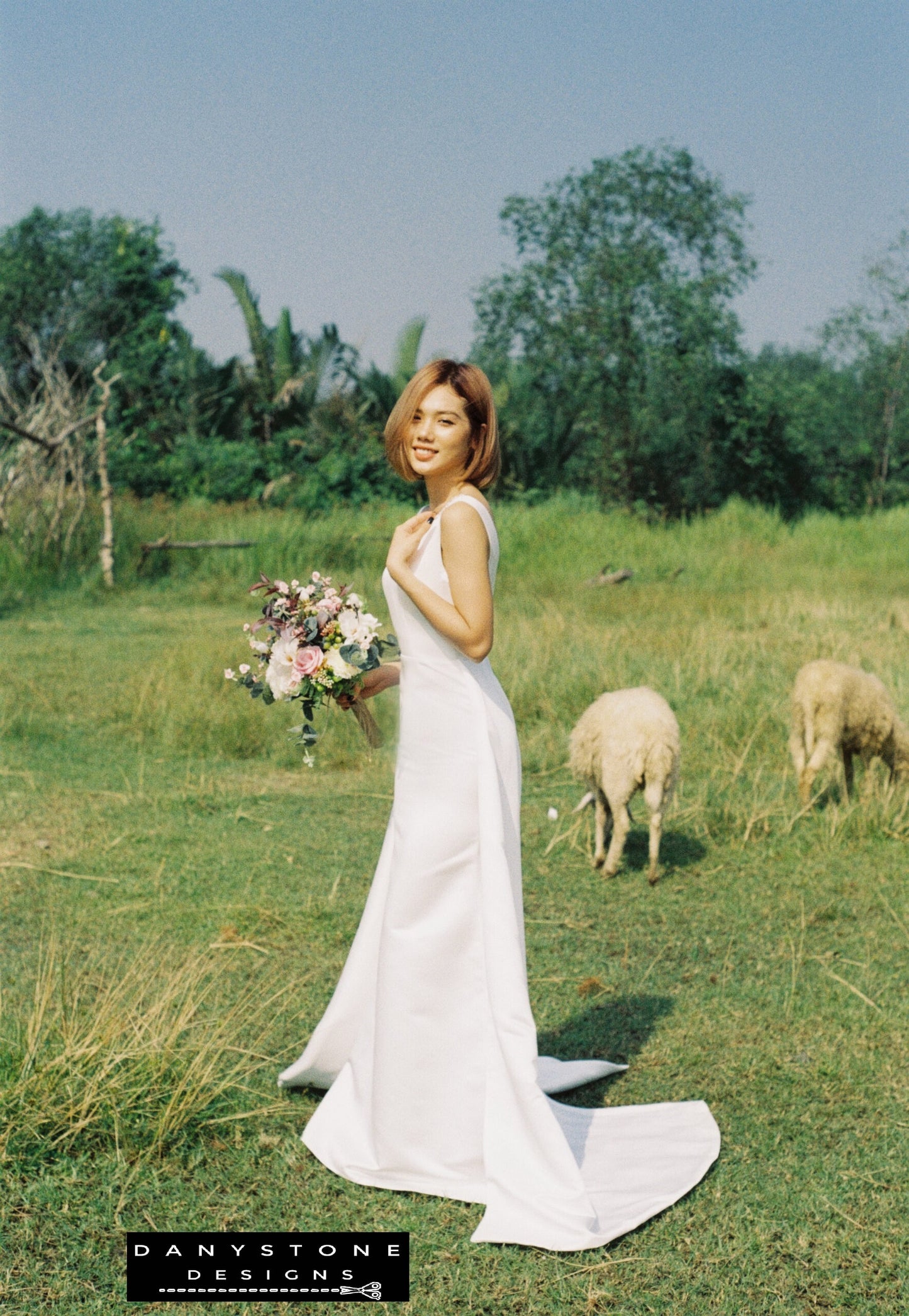 Woman in a white dress holding flowers in a grassy field with sheep