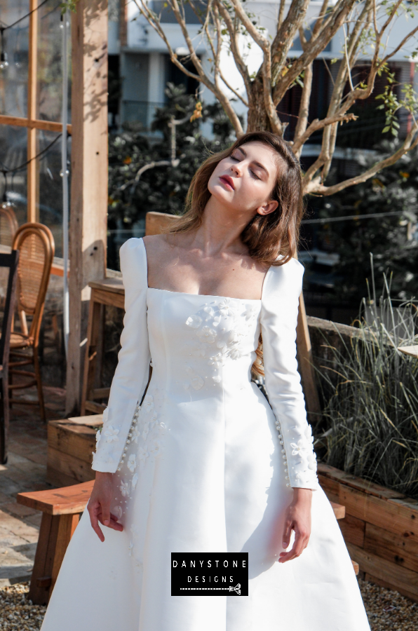 Model posing in an outdoor setting wearing the 7-piece tafta dress with embossed flowers and long sleeves.