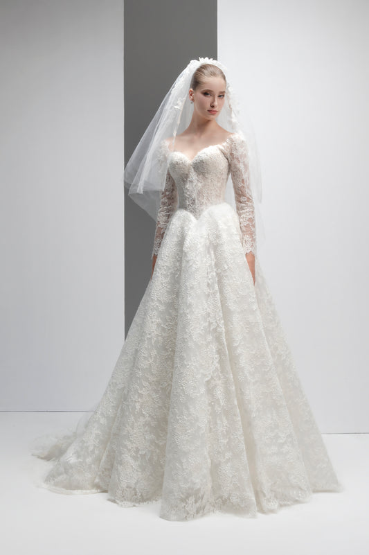 Model wearing a white lace wedding dress with a long train and veil against a plain background