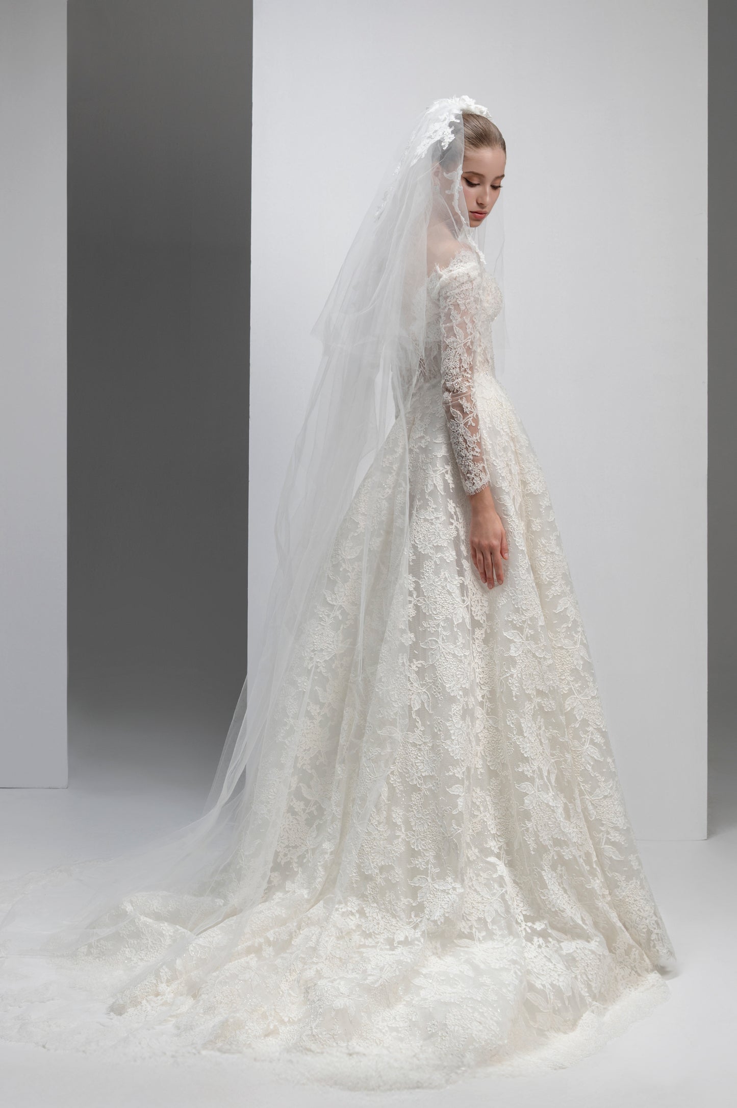 White lace wedding dress with a long veil on a plain background