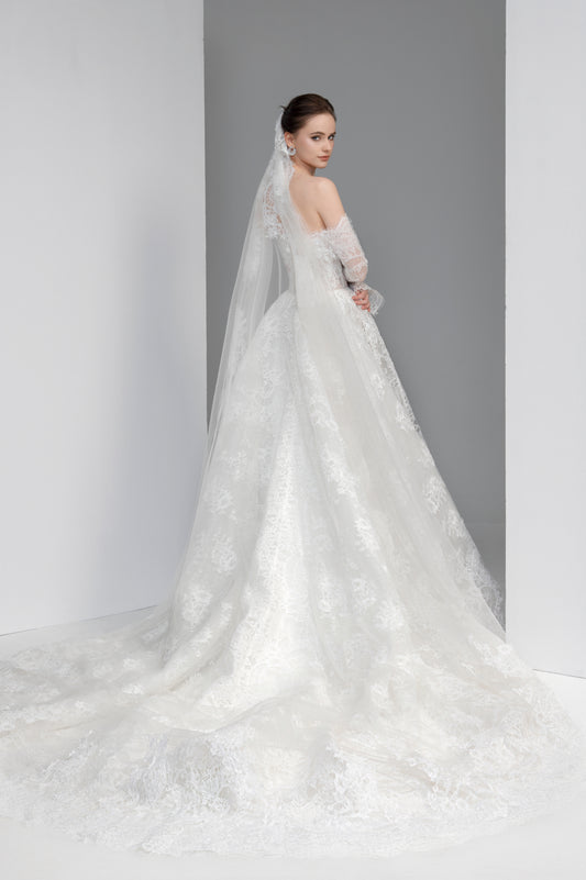 Woman wearing a white wedding dress with a long train and veil against a gray background