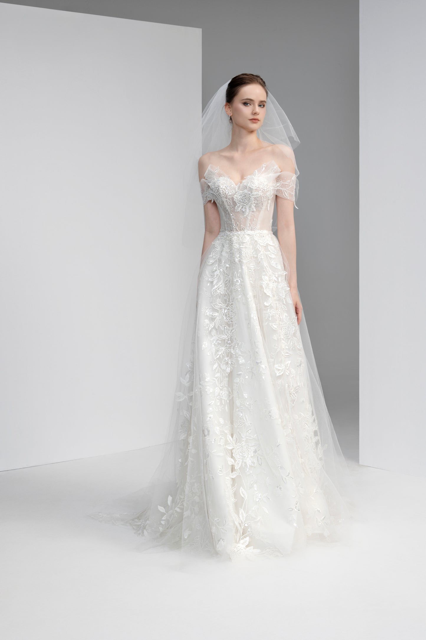 Model wearing a white lace wedding dress with a veil against a plain background