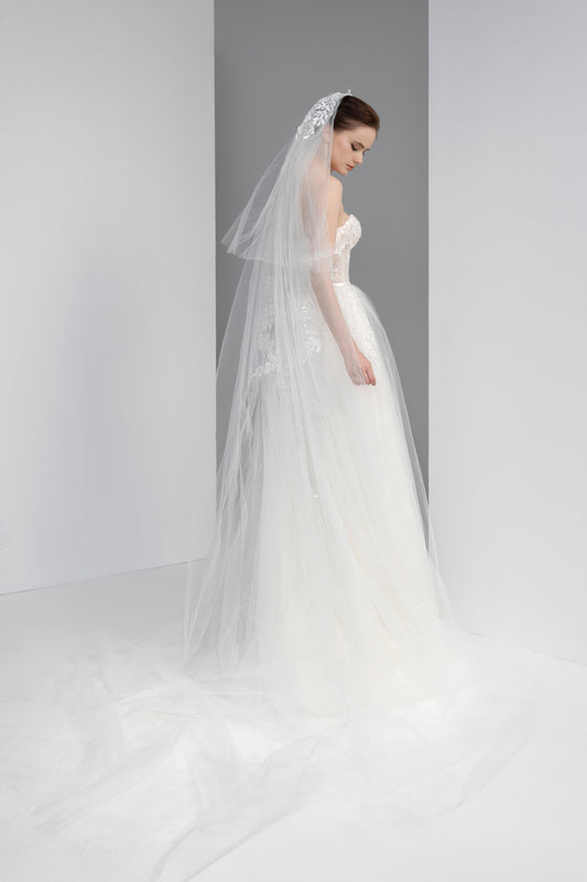 Woman wearing a white wedding dress with a long veil against a gray background