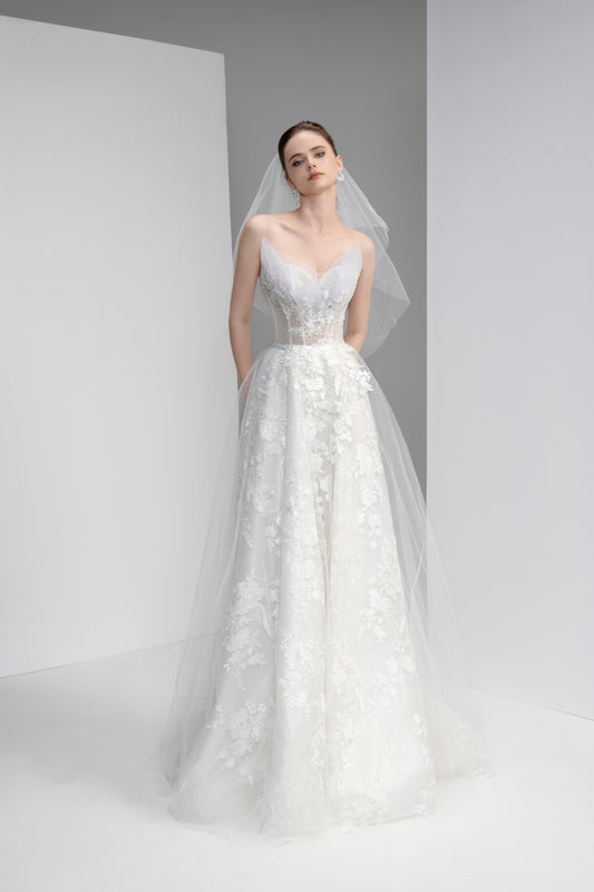 Woman wearing a white wedding dress with floral details against a plain background