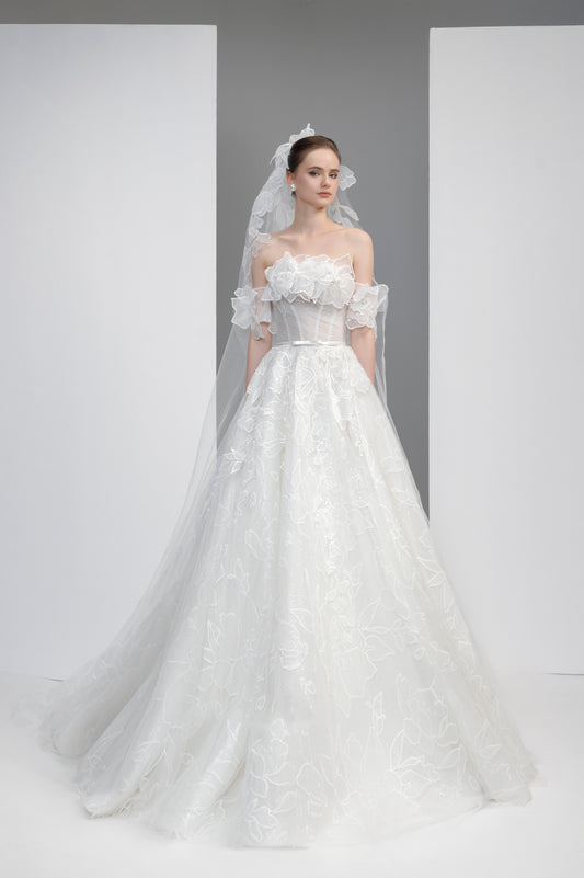 Model wearing a white wedding dress with a veil against a plain background