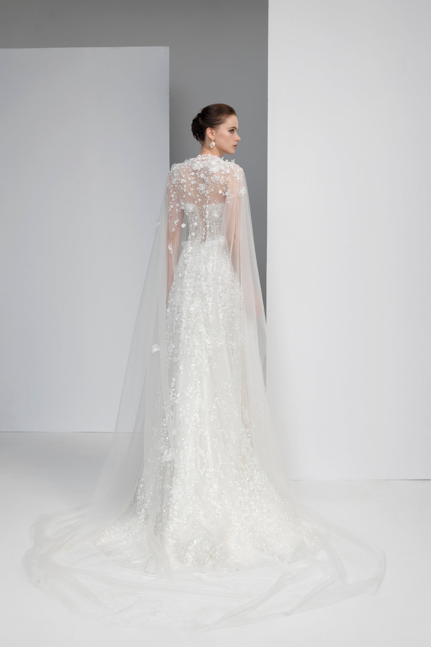 Woman wearing a white wedding dress with a long train and sheer sleeves against a plain background