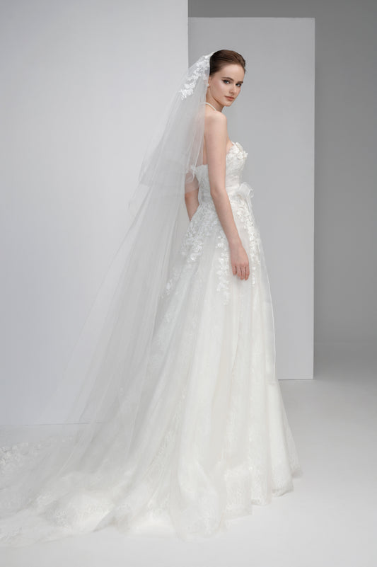 Model wearing a white wedding dress with a long veil against a plain background