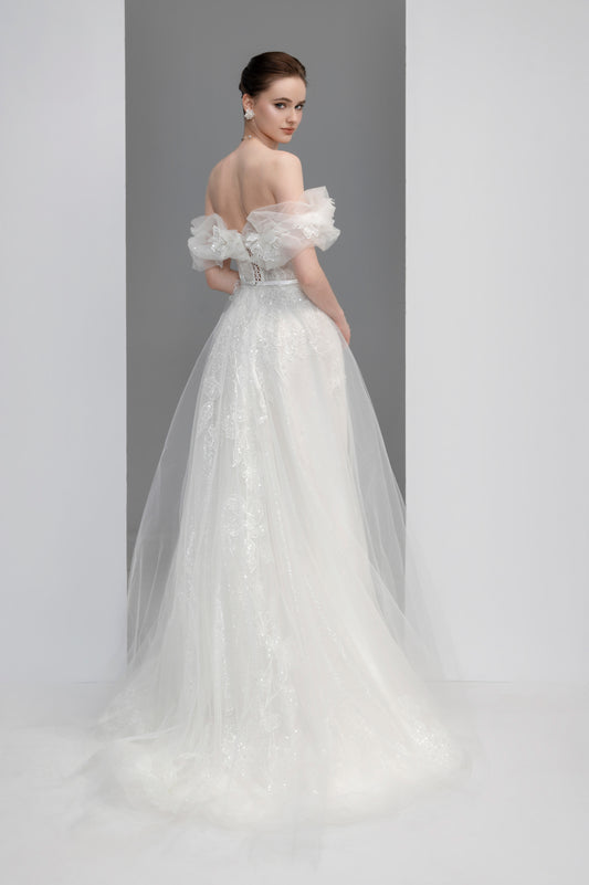 Woman wearing a white wedding dress with ruffled sleeves against a gray background