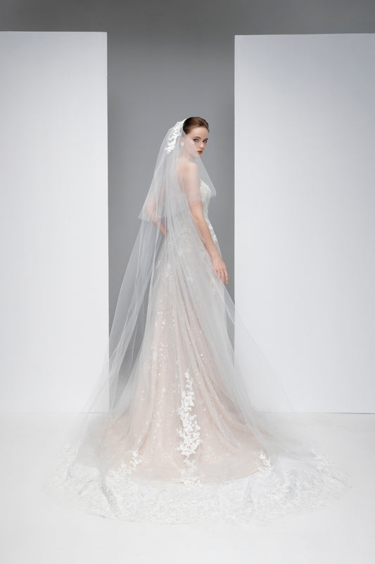 Woman wearing a white wedding dress with a long veil against a plain background