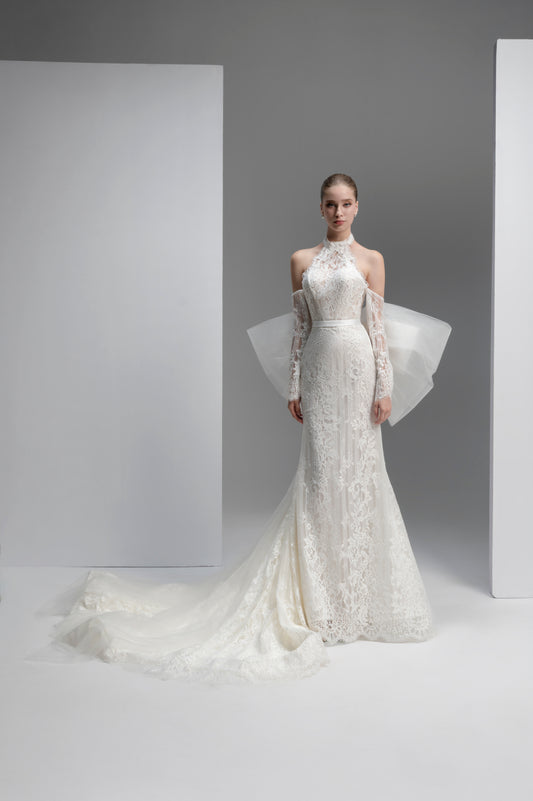 Model wearing a white lace wedding dress with sheer sleeves against a gray background