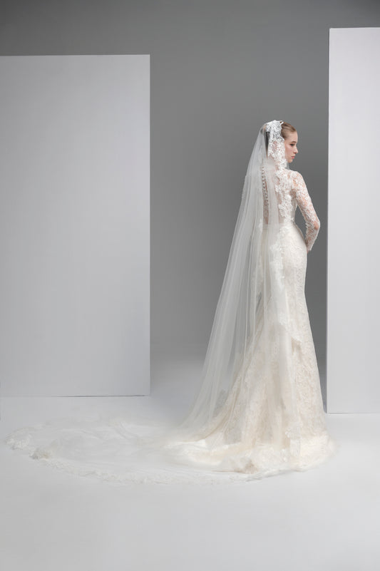 Bride in a white wedding dress with a long veil standing against a plain background