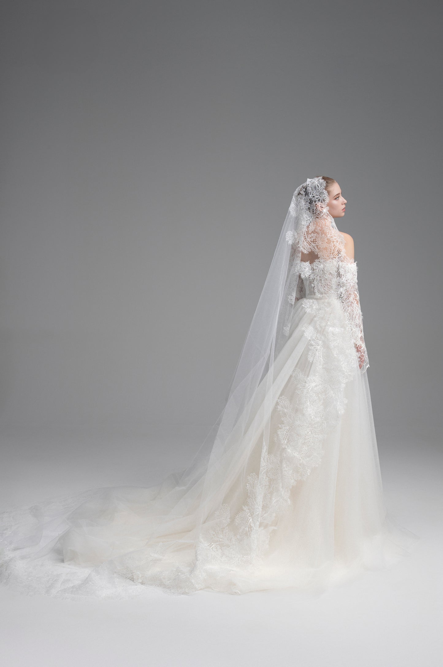 Bride in a white wedding dress with a long veil against a gray background