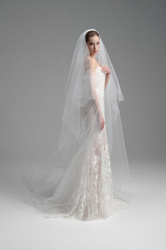 Bride in a white wedding dress with a long veil against a gray background
