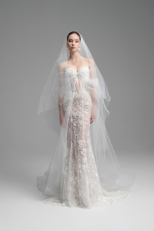 Woman wearing a white lace wedding dress with a long veil on a gray background