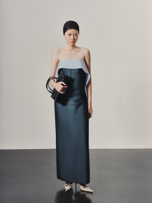 Woman wearing a two-tone dress holding a clutch against a plain background