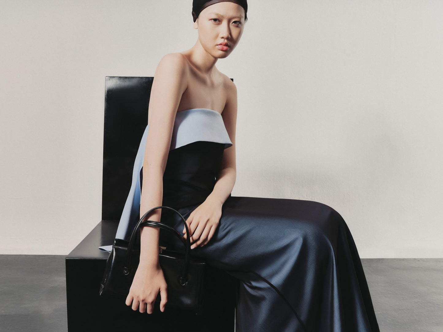 Woman in a stylish outfit with a black bag against a neutral background