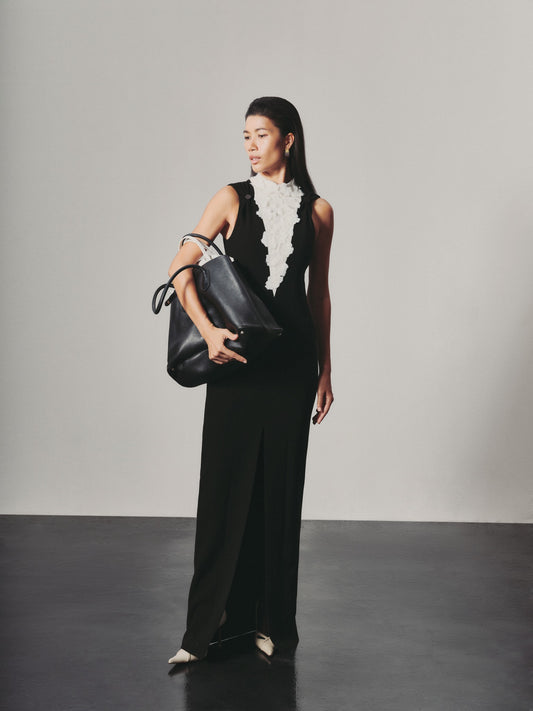 Woman holding a black handbag against a plain background