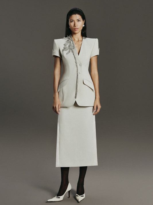 Woman wearing a light gray suit with a floral embellishment on a gray background