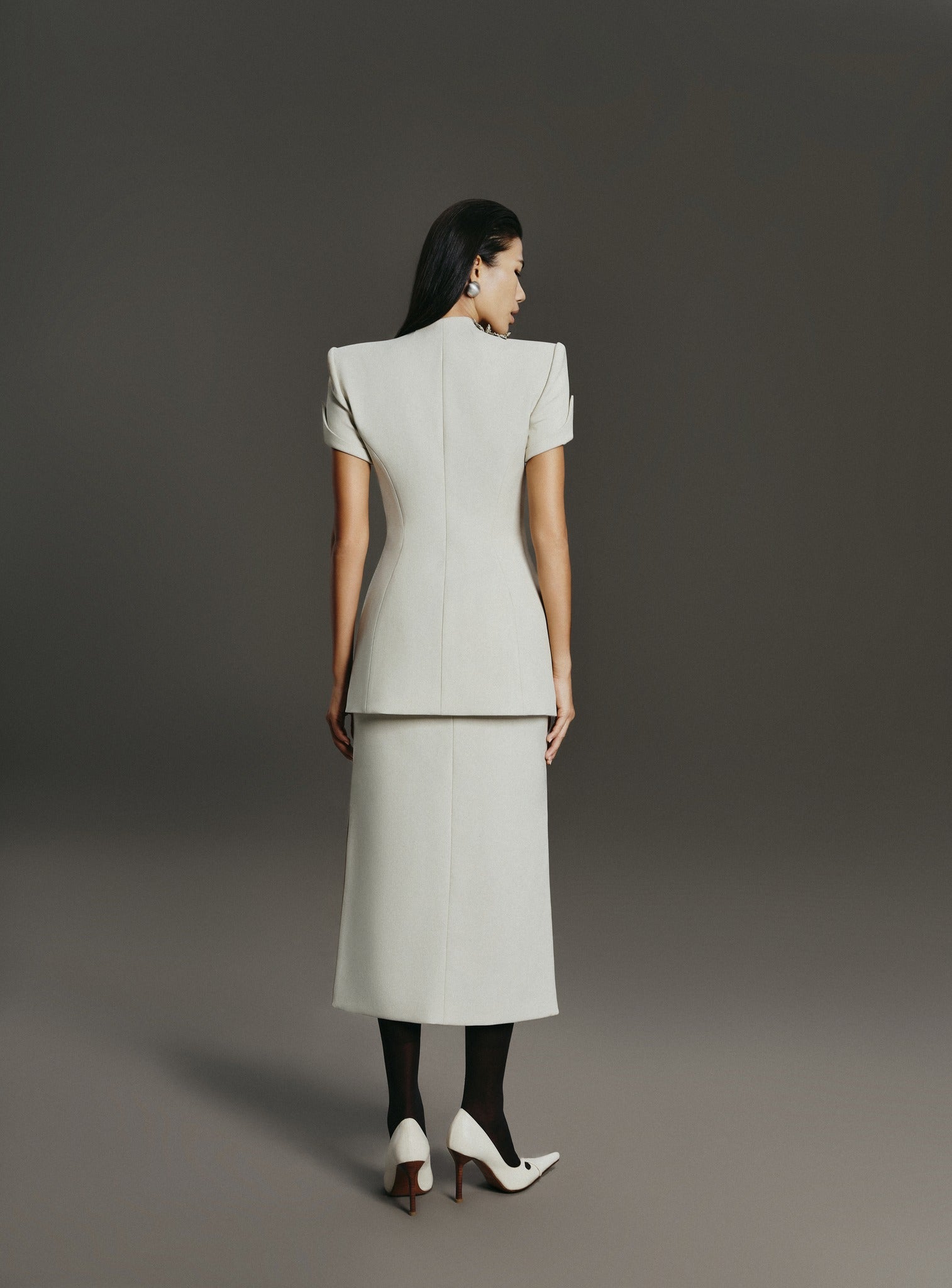 Woman wearing a light gray suit standing against a plain background