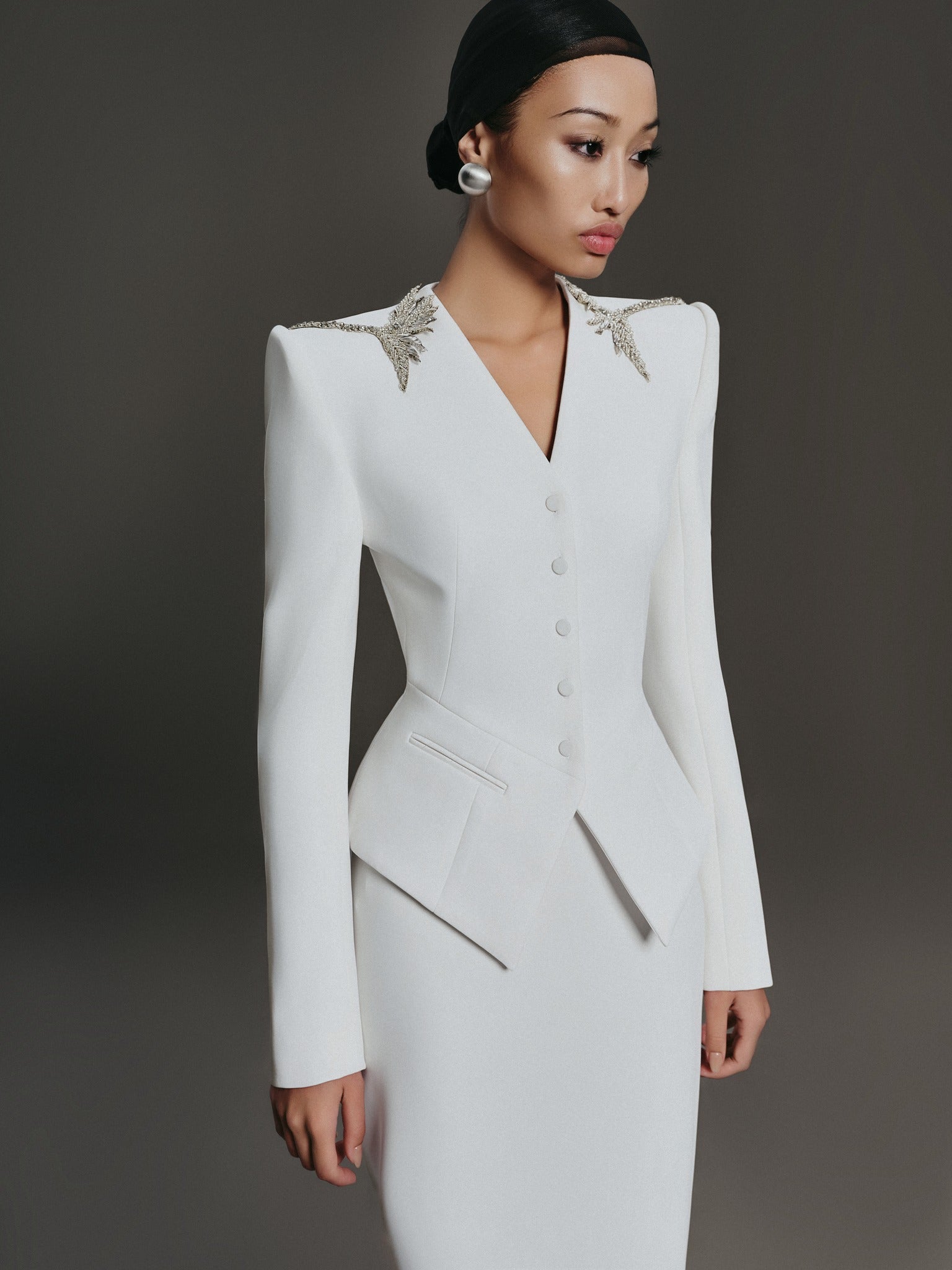 White formal dress with intricate shoulder detailing on a dark background