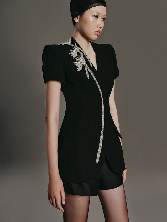 Model wearing a black outfit with feather details on a gray background