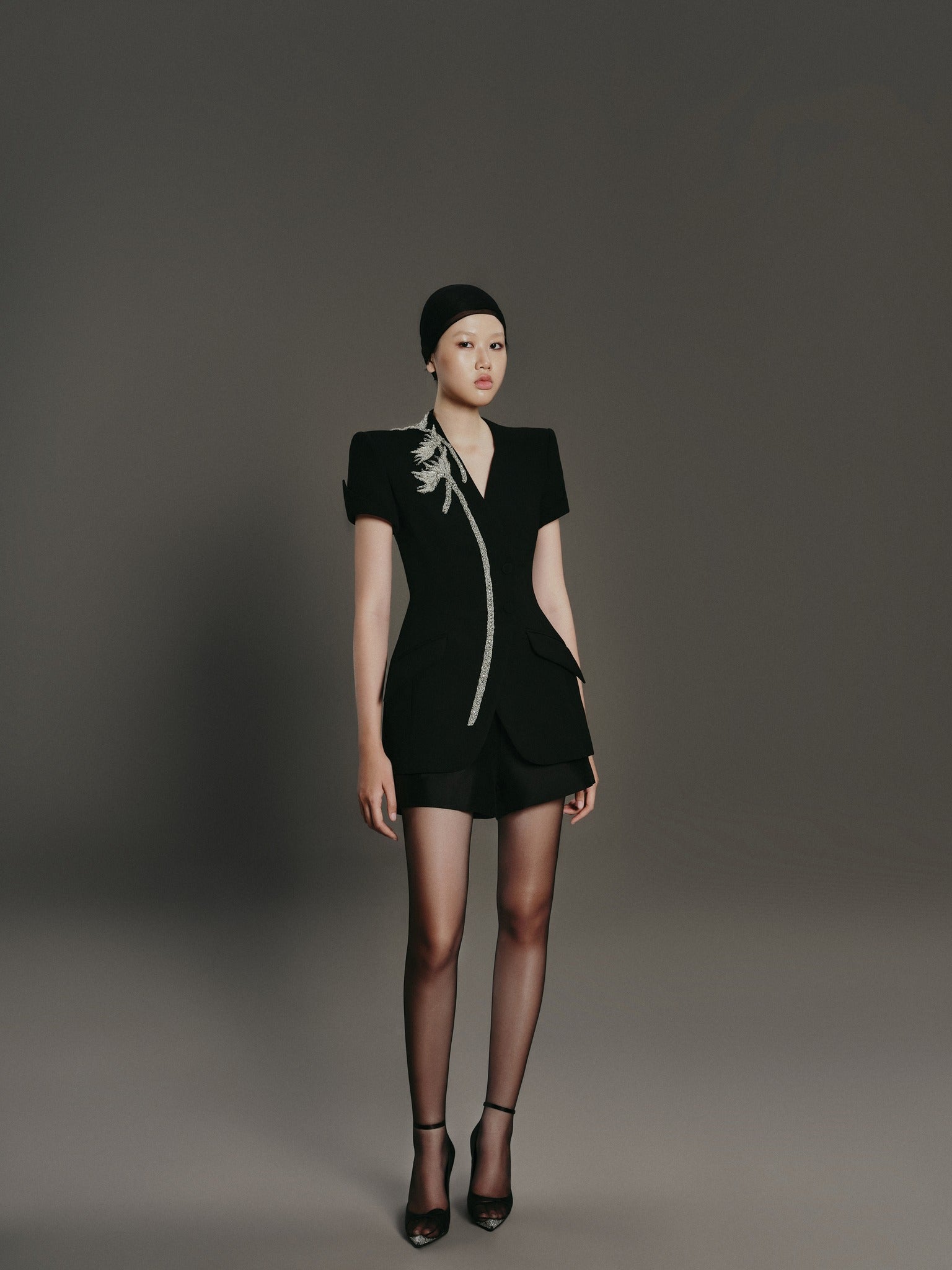 Model wearing a black outfit with a floral detail on a gray background