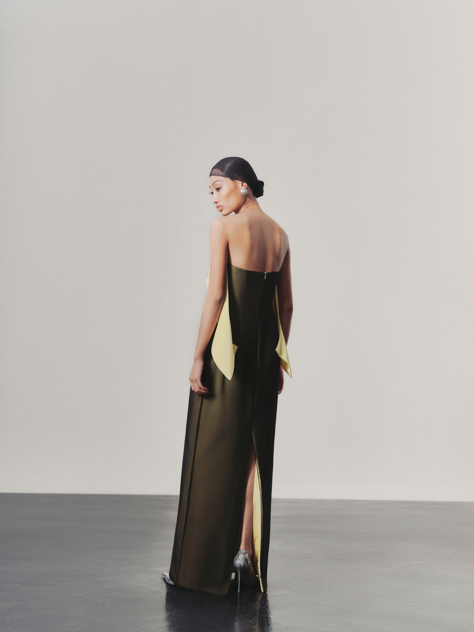 Woman wearing a long, elegant dress with a yellow accent on a plain background