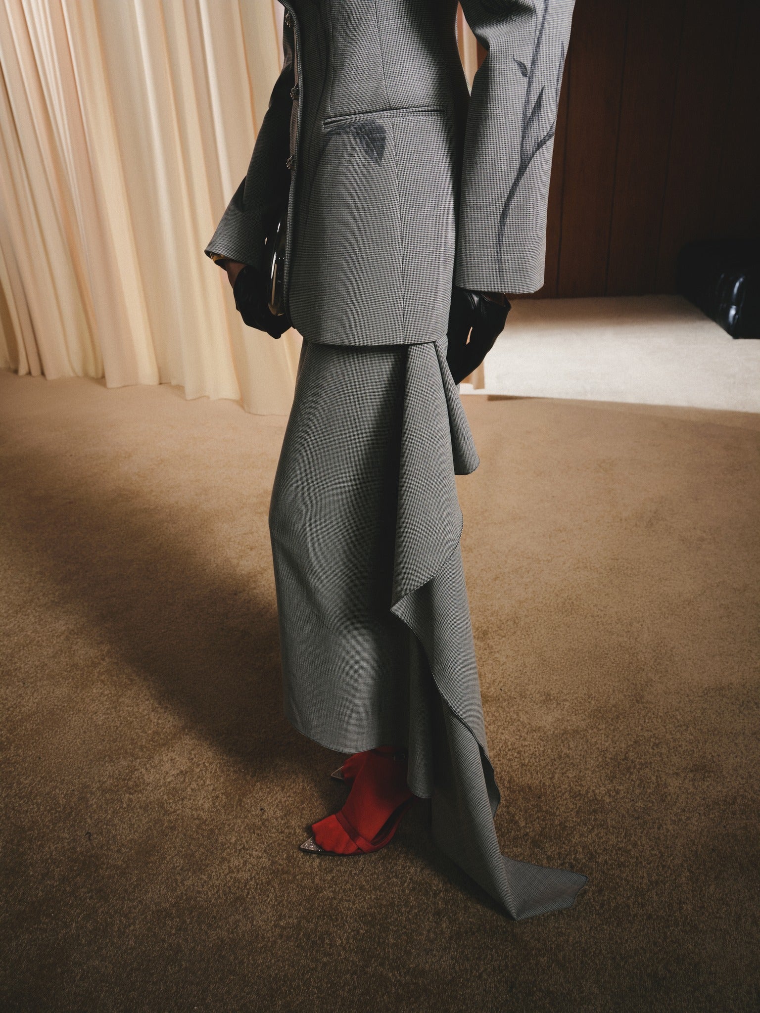 Person wearing a gray suit with a ruffled skirt on a brown floor.