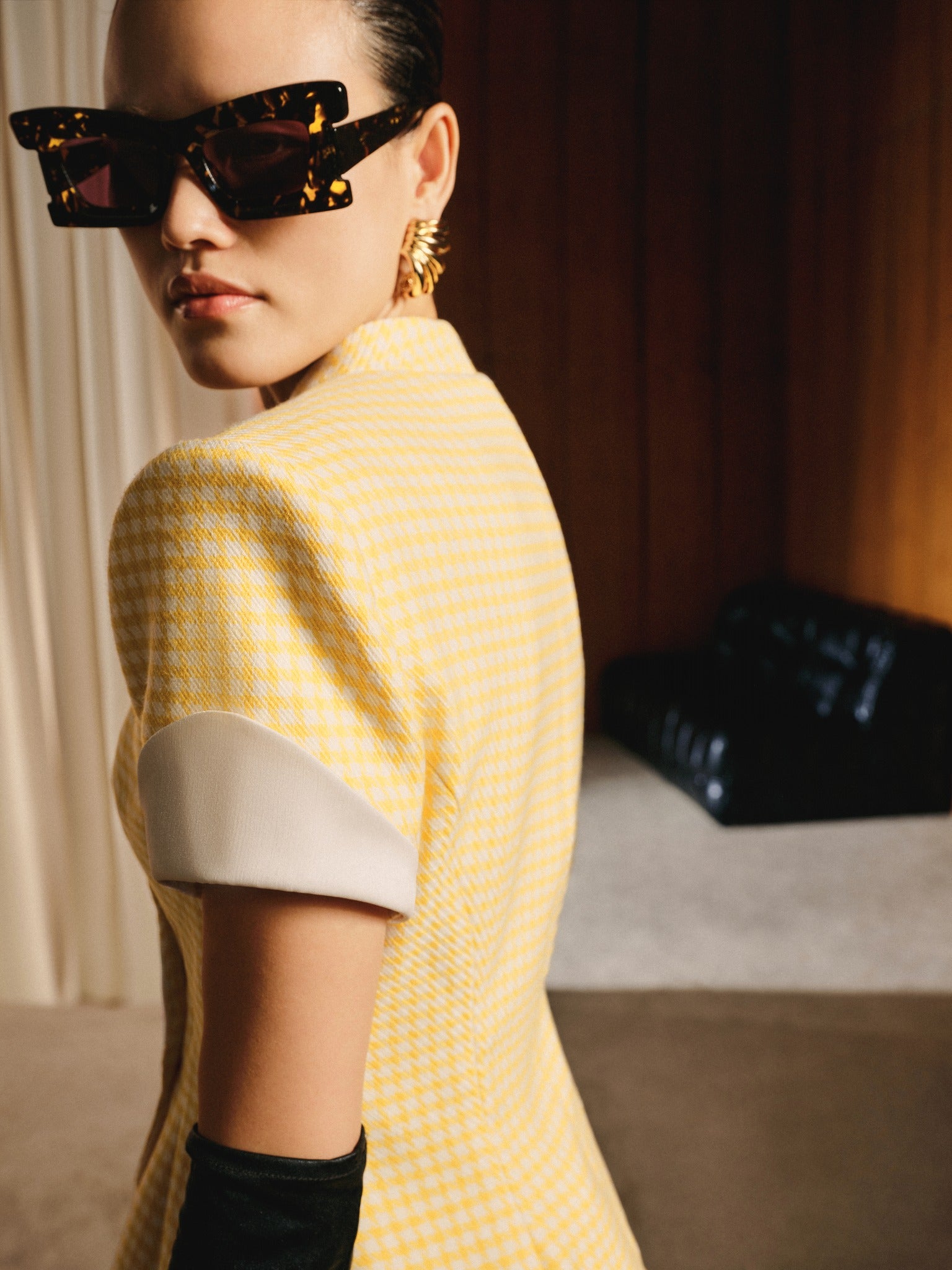 Woman wearing a yellow patterned dress with a black handbag in the background