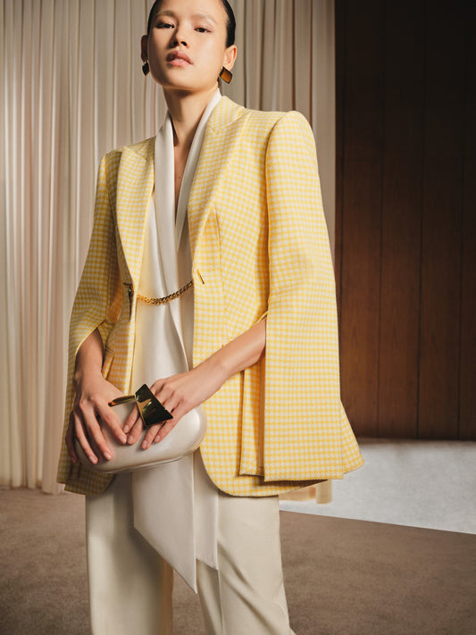 Woman wearing a yellow checkered blazer over a white top, holding a clutch.