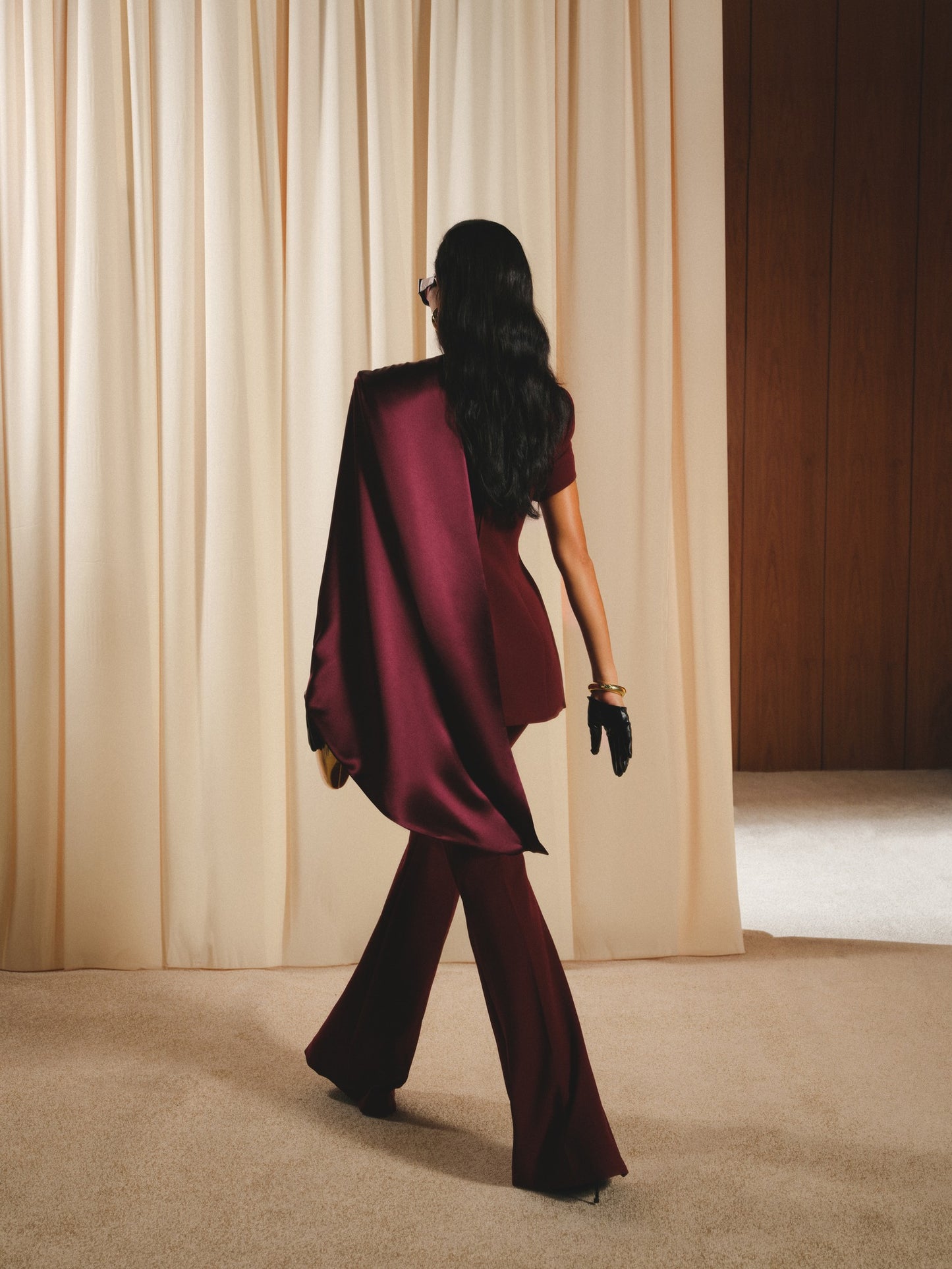 Woman in a burgundy outfit walking towards a curtain