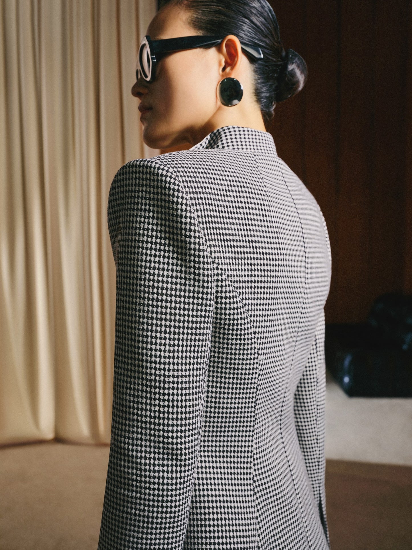 Person wearing a black and white checkered blazer in an indoor setting.