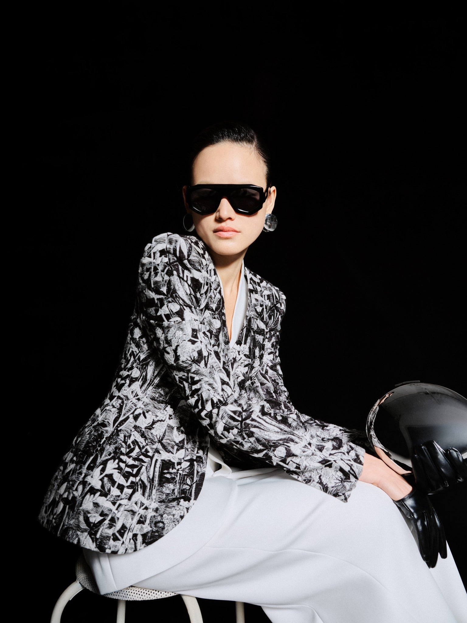 Person wearing a patterned blazer and sunglasses against a black background