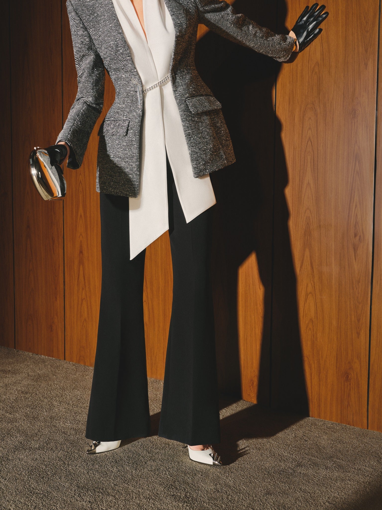 Person wearing a gray blazer, white shirt, and black pants against a wooden panel background