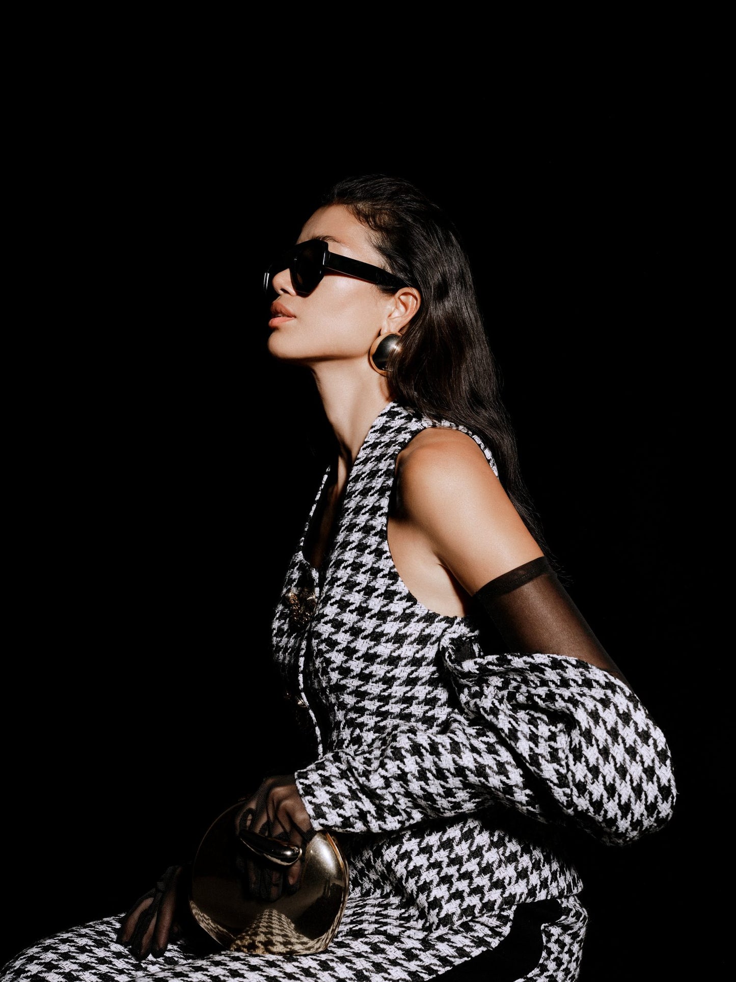 Woman wearing a black and white patterned outfit with sunglasses against a dark background