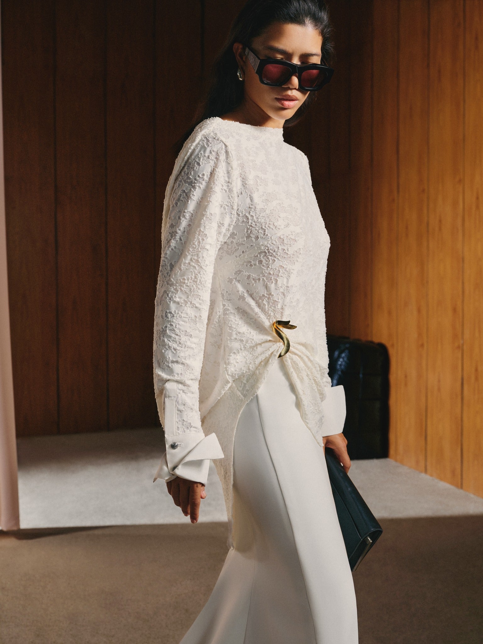 Woman in a white lace top and pants walking indoors.