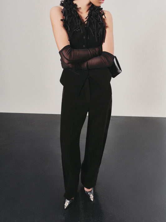 Person wearing a black outfit with sheer sleeves and high heels on a plain background