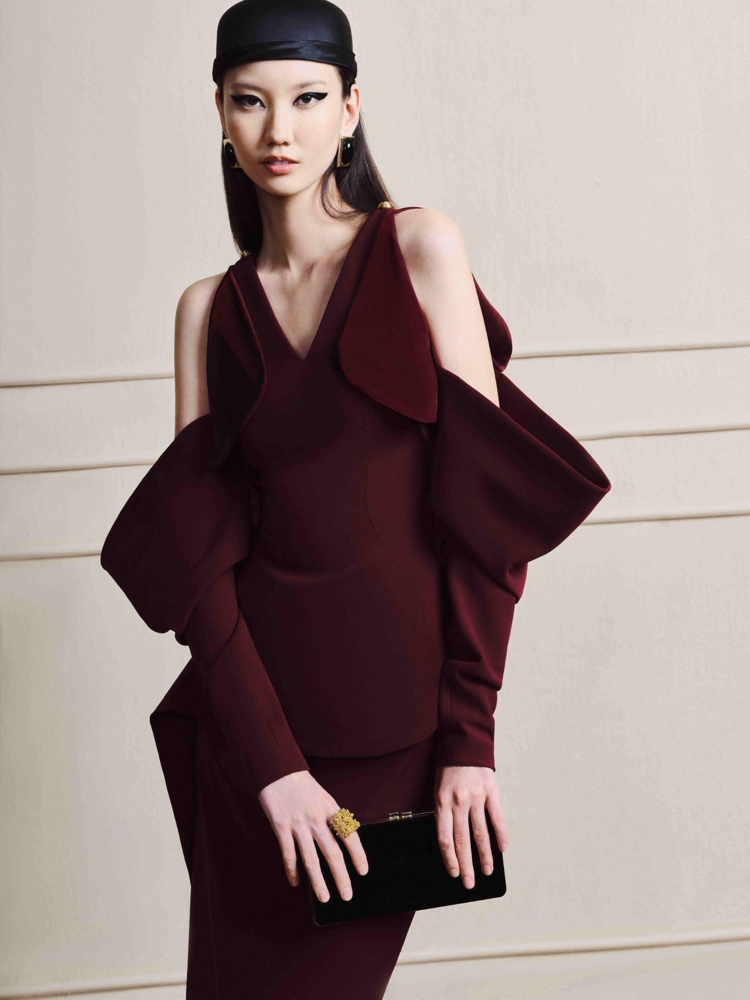 Woman wearing a burgundy dress with a black clutch against a neutral background