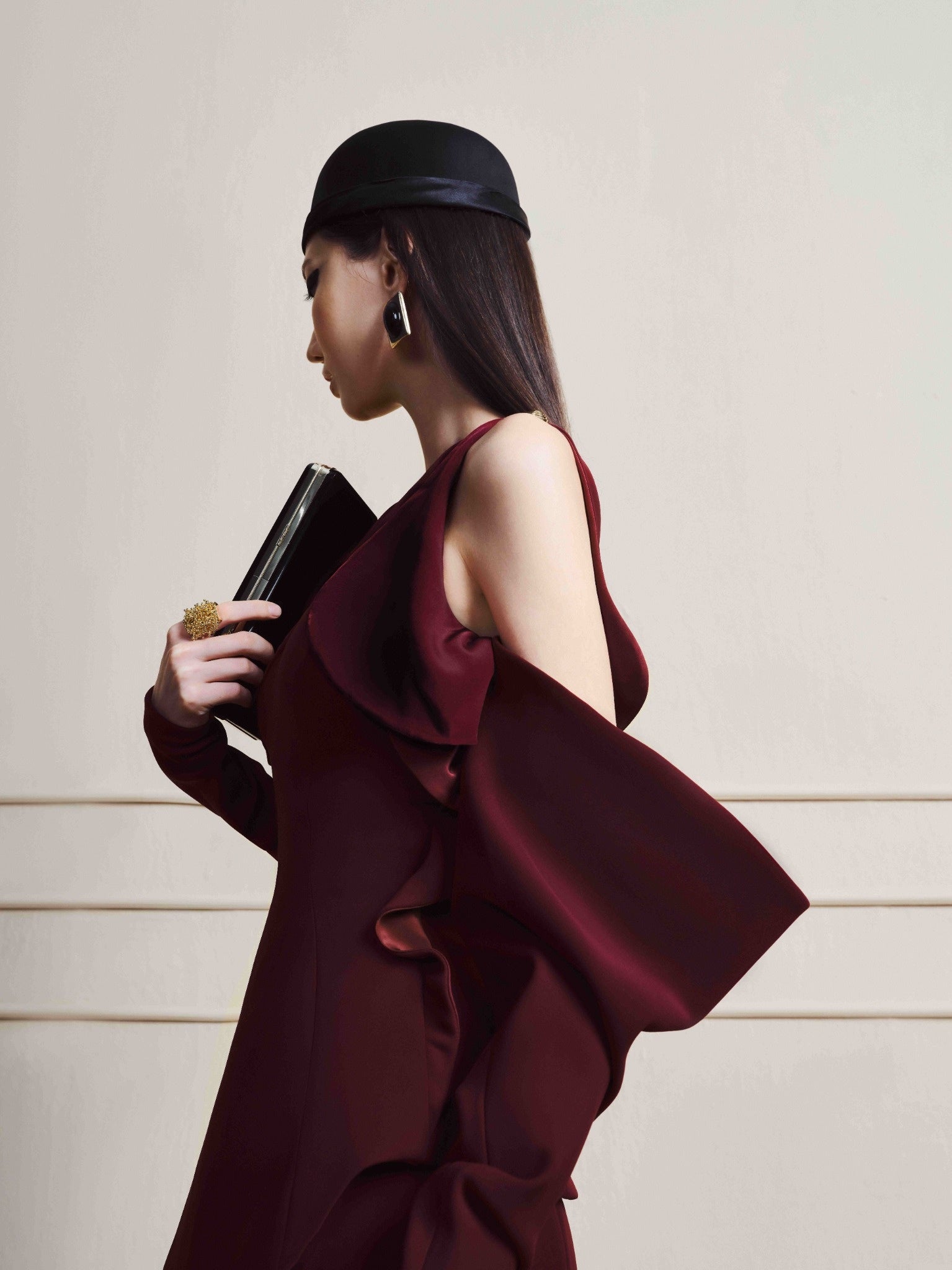 Woman in a burgundy dress holding a black clutch against a neutral background
