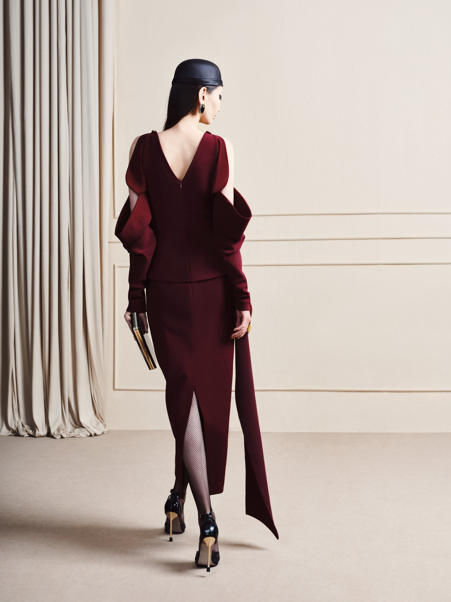 Woman in a burgundy dress with a high slit, standing in a minimalistic room.