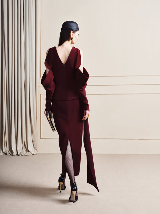 Woman in a burgundy dress with a high slit, standing in a minimalistic room.