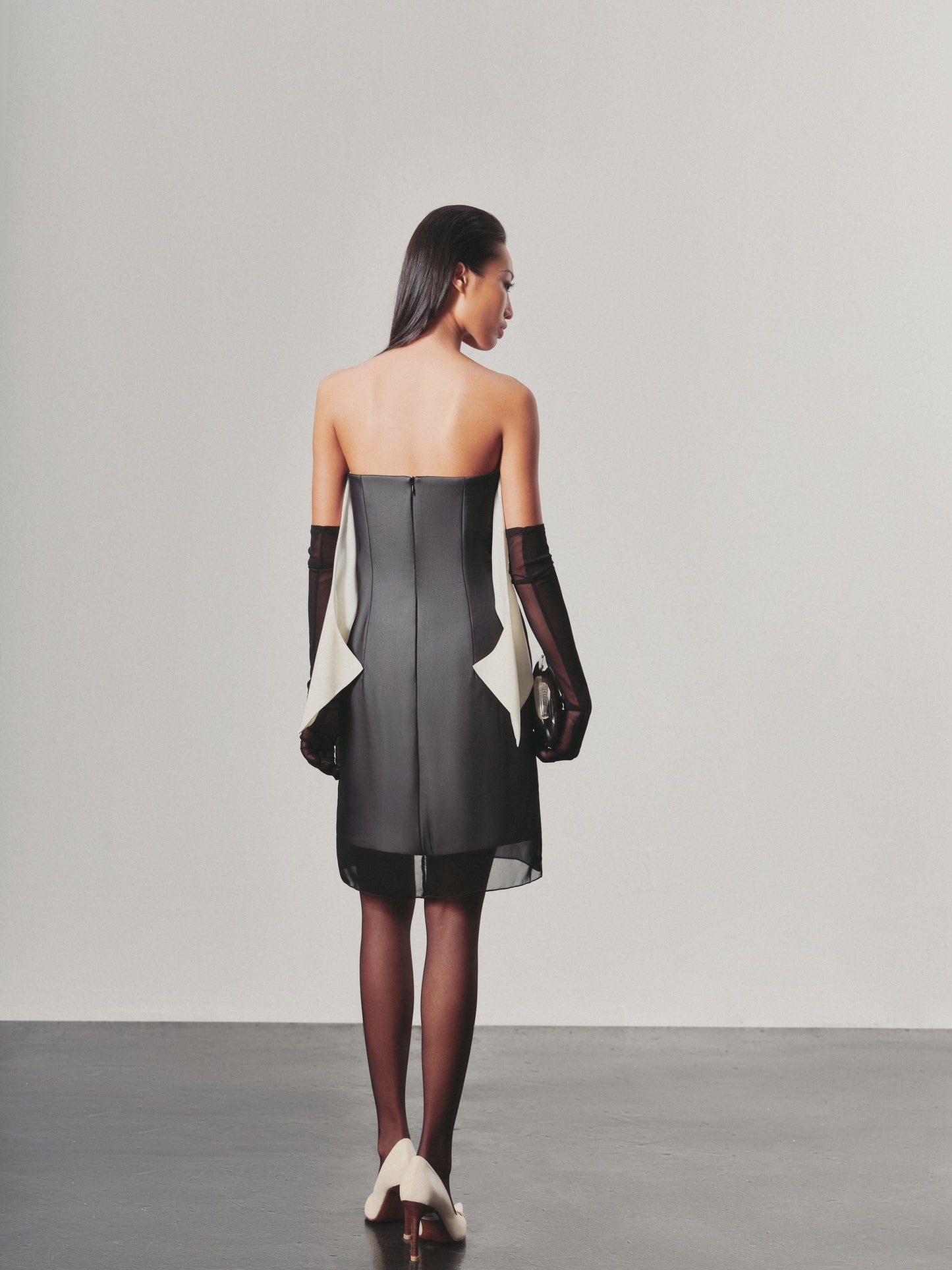 Woman wearing a black and white dress with long gloves against a plain background