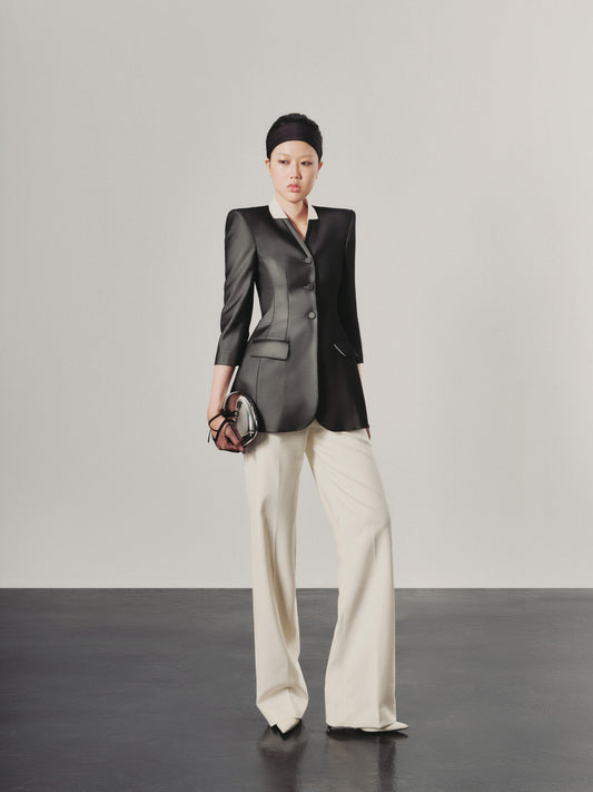 Person wearing a black blazer and white pants against a plain background