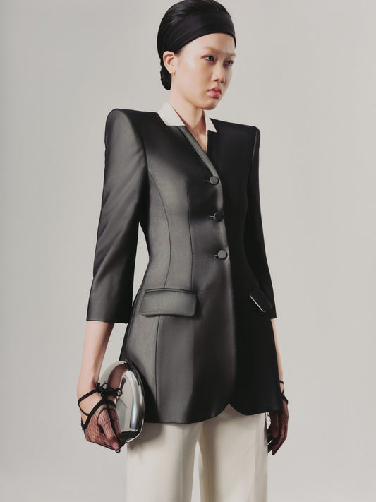 Woman wearing a black blazer and white pants against a plain background