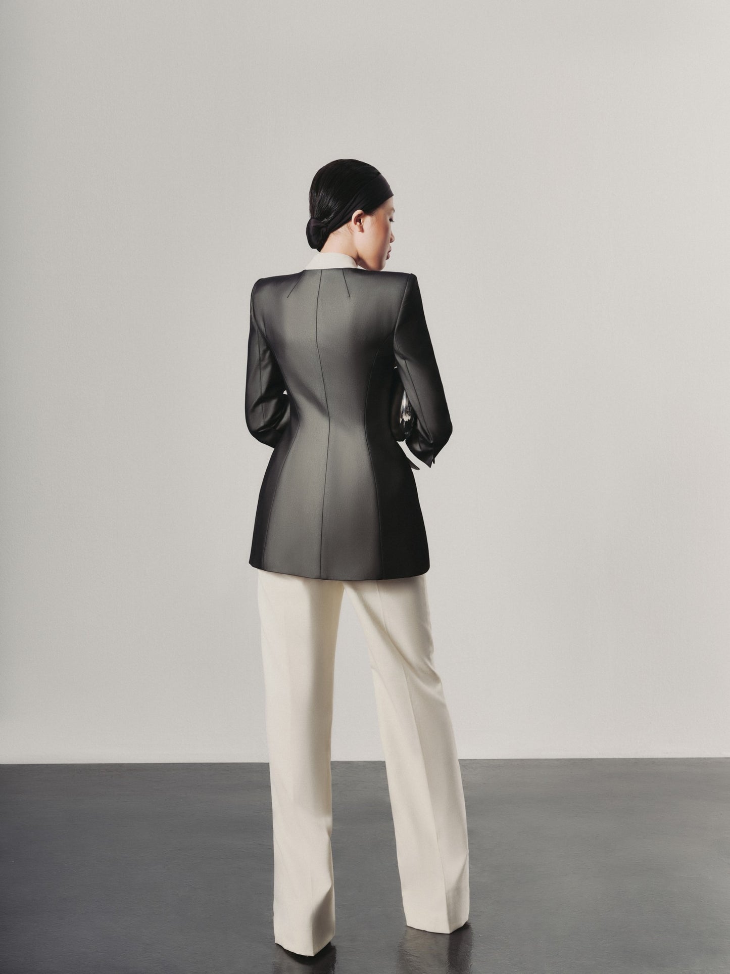 Person wearing a black jacket and white pants against a plain background