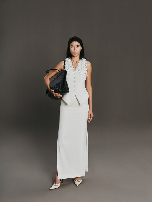 Woman in a white outfit holding a black handbag against a gray background