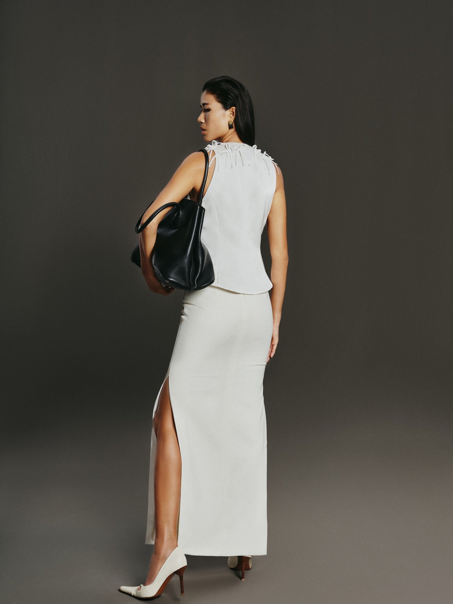 Woman in a white dress with a black handbag against a gray background