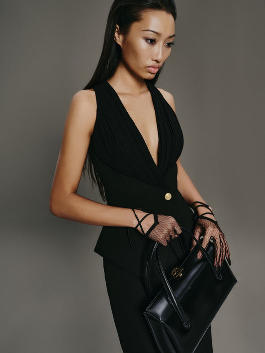 Woman in a black outfit holding a black handbag against a gray background