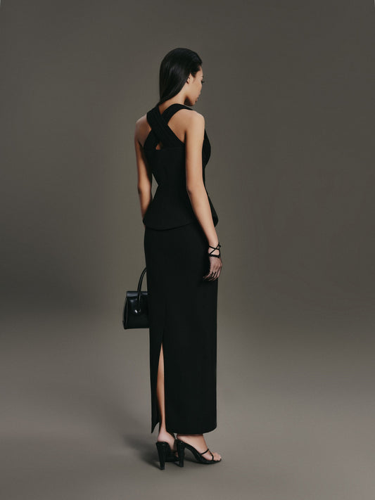 Woman in a black dress with a high slit, holding a matching handbag against a gray background