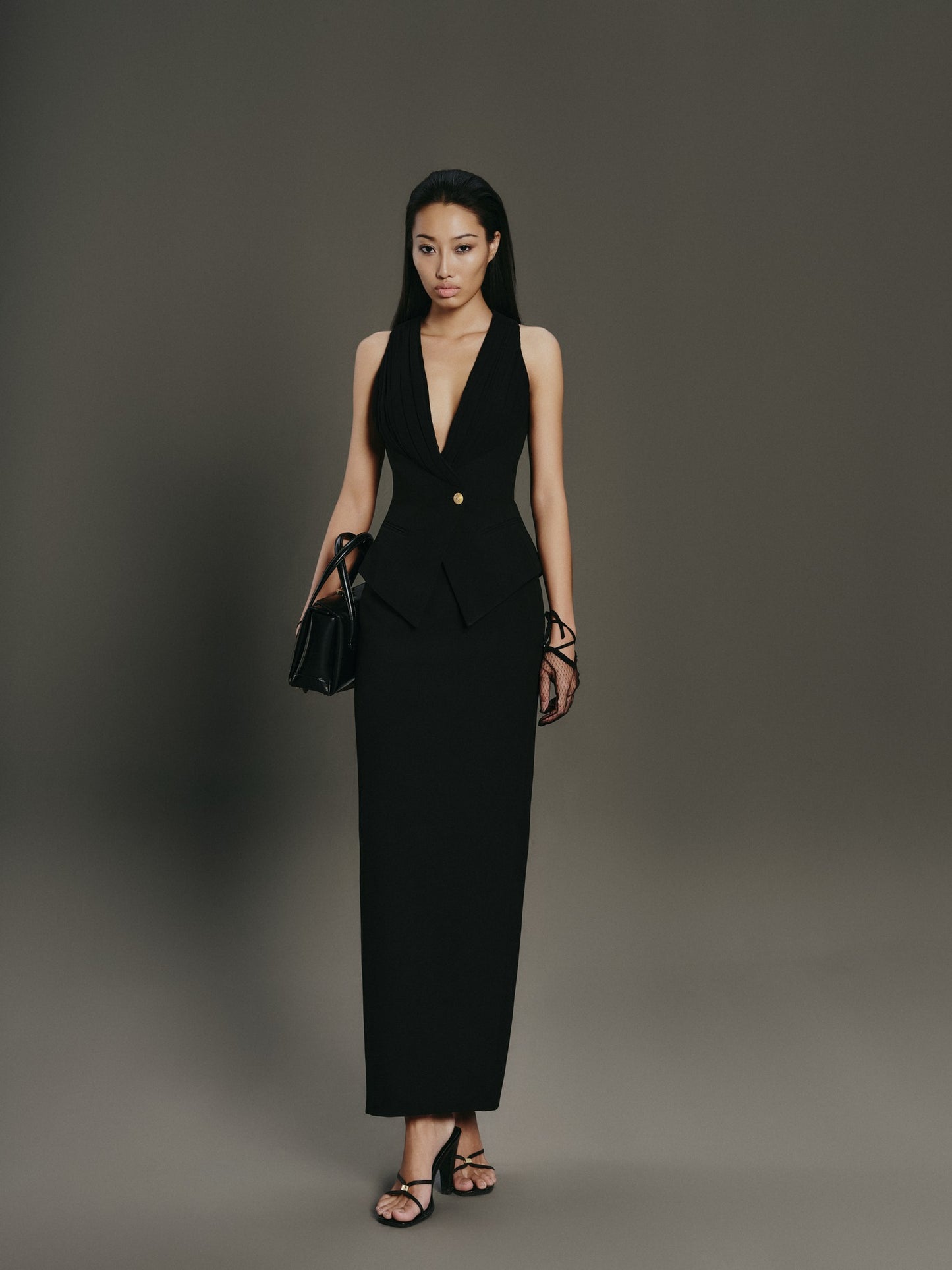 Woman wearing a black suit with a plunging neckline against a gray background